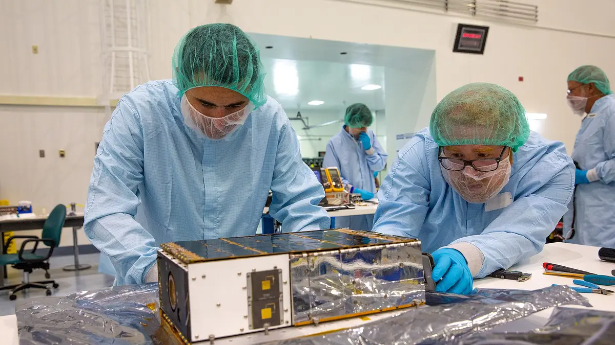 Gowned workers inspecting a foil-faced instrument housing in a cleanroom